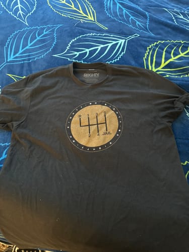 Customer's black 80Eighty® 6Speed = Jail Shirt with the gear shift graphic laid flat on a patterned blanket.