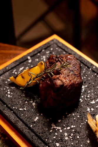 Cliente mostrando su filete cabrería sin hueso asado, servido en una plancha de piedra con romero.
