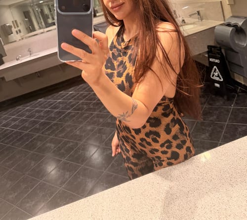 Partial view of a reviewer wearing the leopard print Naked Print Halter Jumpsuit in a bathroom selfie.