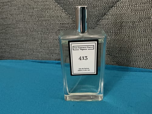 Customer's clear glass bottle of Inspired by Thai Lime and Mango - 413 perfume, sitting on a blue surface.