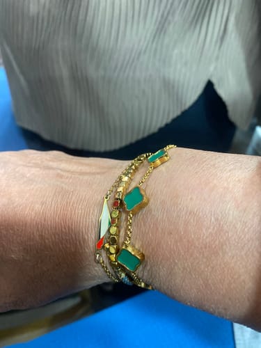 Close-up of a customer's wrist wearing the gold Celine Clover Bracelet with green motifs, stacked with other bracelets.