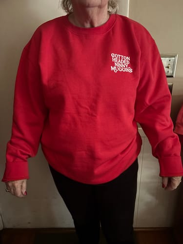 Reviewer showing the fit of their roomy, red 'Cotton Headed Ninny Muggins' sweatshirt.