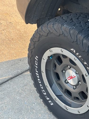 A customer's bright teal valve stem cap installed on a car's tire and rim.
