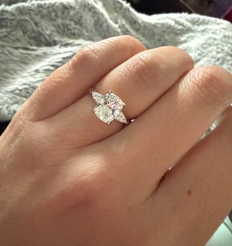 Customer's hand wearing their custom DovEggs lab-grown diamond ring with a cushion cut center stone and two side stones.