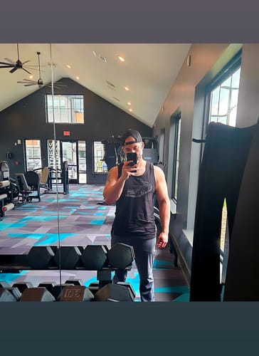 Customer taking a mirror selfie at a gym in the black 80Eighty® Frontline Tank.