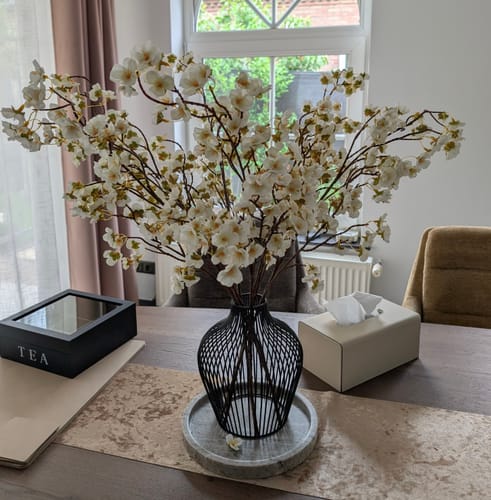 Recensents moderne, zwarte Mia Vaas gevuld met witte bloesem op een eettafel.