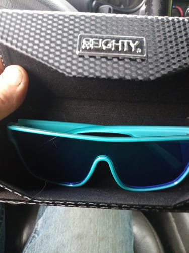Customer holding open the branded black case to show the teal 80Eighty Polarized Bay Sunglasses inside.