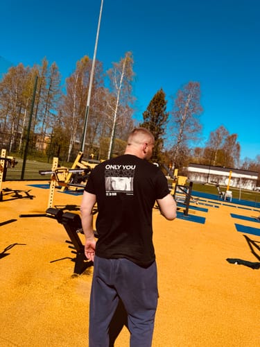 Ein Kunde von hinten, der das schwarze T-Shirt 'Only you' in einem Fitnesspark im Freien trägt und den Rückendruck zeigt.
