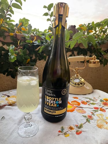 Reviewer's bottle of Sparkling wine next to a filled crystal glass on a porch.