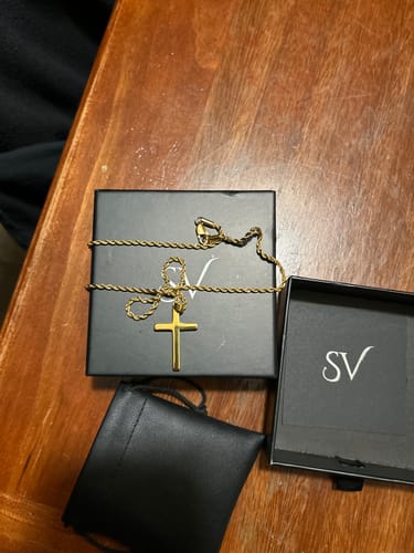 Reseñador mostrando el Crucifix Pendant Oro en su caja negra de presentación.