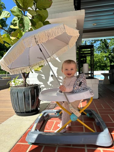 Customer's Off-White Mini Umbrella with fringe attached to a baby's walker on a patio.