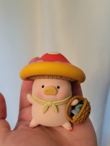 Customer holding the detailed Lulu The Piggy figurine in their palm. It has a red mushroom cap, a yellow scarf, and a small basket.