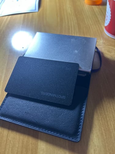 Customer's black SPOTMINDERS Tracking Card shown partially inserted into a black wallet on a table.
