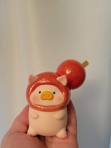 Customer holding a LuLu the Piggy figurine with a sparkly red hood and a candied fruit accessory on its head.