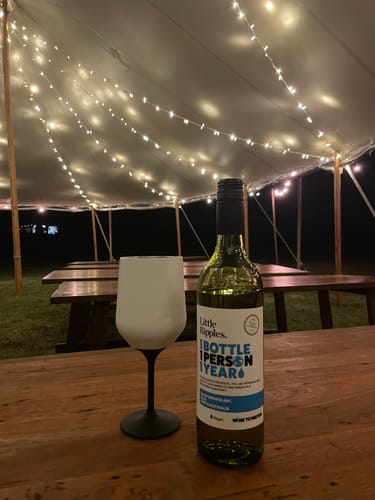 Customer's bottle of Sauvignon Blanc and a wine glass on a table under a tent lit by warm fairy lights.