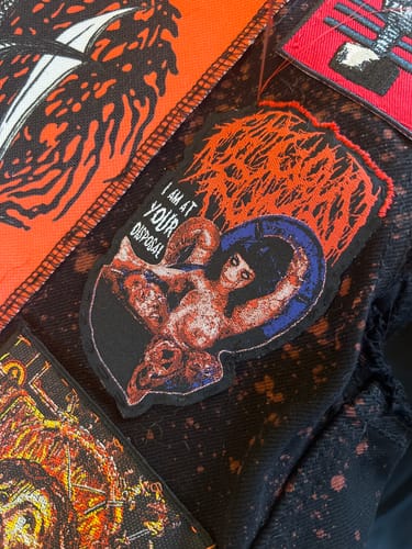 Customer's Fatuous Rump patch being sewn with a red border onto a black, bleach-splattered jacket.