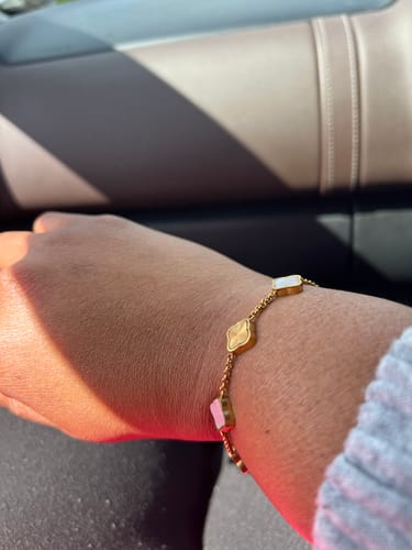 Close-up of a reviewer wearing a gold-colored bracelet with white and gold clover-shaped charms.