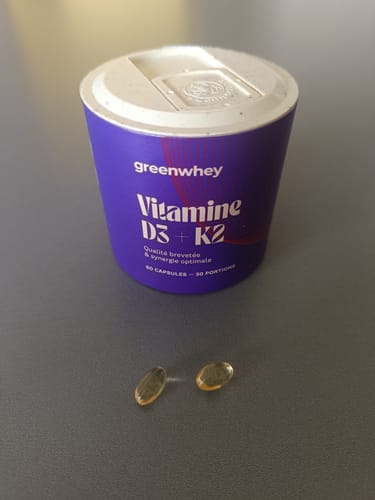 Le pot violet de Vitamine D3 + K2 du client, avec deux gélules dorées sur une table.