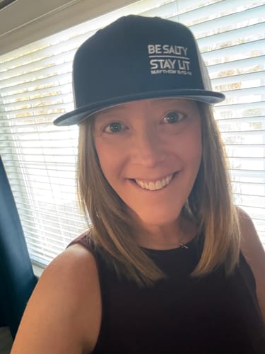 Customer smiling while wearing the black Be Salty Stay Lit hat with a flat brim.