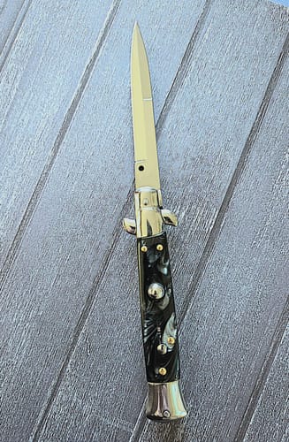 Reviewer's Italian Style Push Button Switchblade with a black marble handle, open on a grey wood surface.