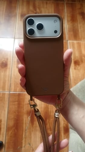 Primeiro plano da mão de um cliente segurando um celular com a Cordinha Nora Mocha Mousse, mostrando seus ganchos dourados.