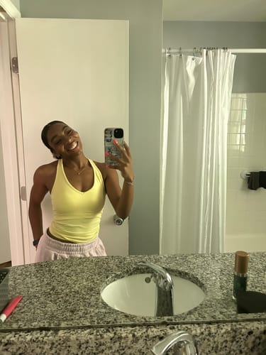 Customer taking a selfie in a bathroom wearing the yellow Curve Seamless Tank.