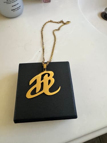 Customer's gold-colored custom initial pendant necklace resting on its black gift box on a white counter.