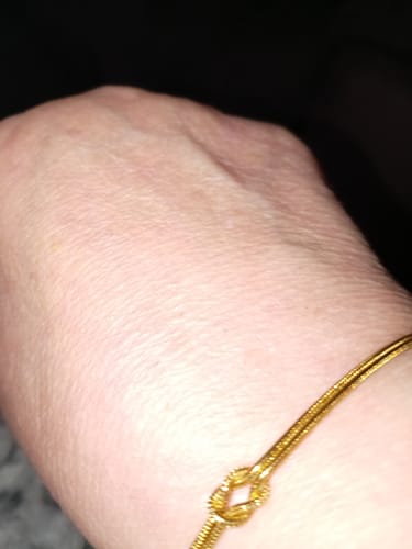Close-up: Customer's gold Forever Knot Bracelet on their wrist.