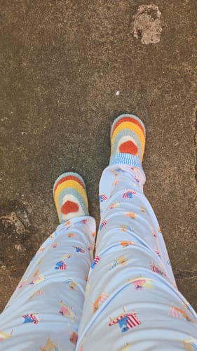 A top-down view of a customer wearing the colorful Plush Rainbow Heart Slippers with patterned pants.
