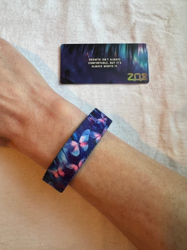 Reviewer's Change Is Beautiful Bracelet with a butterfly pattern on their wrist, next to its inspirational card.