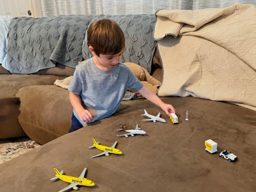 A child playing with the colorful SPIRIT AIRLINES PLAYSET spread out on a brown couch.