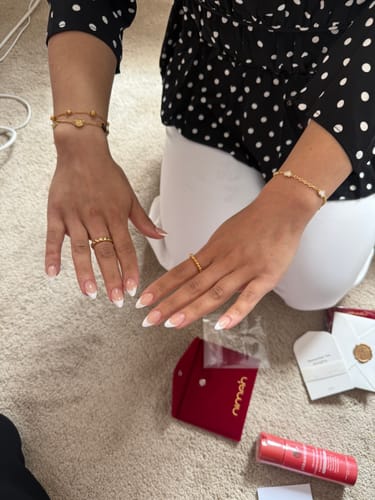 Reviewer wearing two gold Happiness Bracelets on their wrists, with product packaging on the floor.