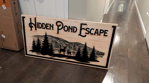 Customer's personalized Family Mountain Sign with 'Hidden Pond Escape' text and a rustic mountain scene, placed on a floor.