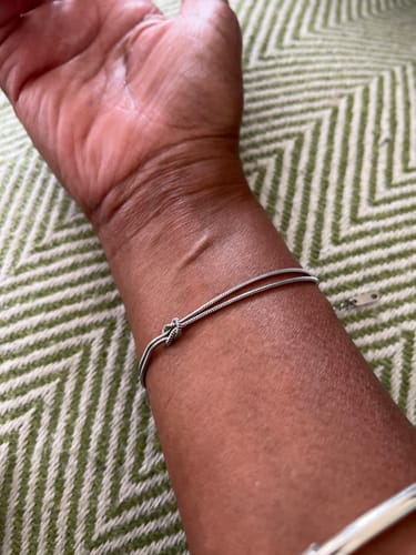Close-up of a reviewer's wrist wearing a thin, silver-colored bracelet with a knot.