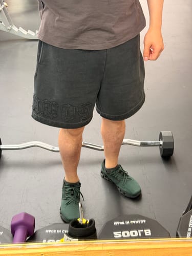 Customer showing the baggy fit of the dark Patchwork Shorts with lettering detail at the gym.