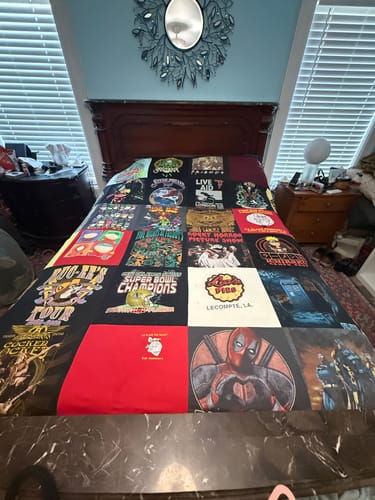 Customer's completed Project Repat T-Shirt Quilt, featuring numerous graphic shirts, displayed on a bed.