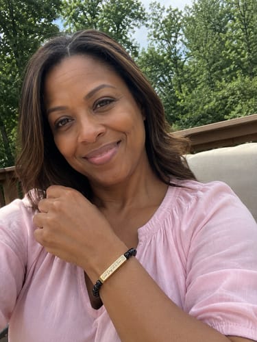 Reviewer smiling while wearing her black and gold One Day at a Time Bracelet outdoors.