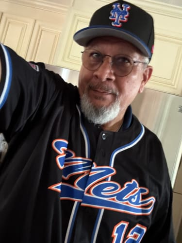 Close-up of a customer smiling while wearing the custom black baseball jersey with blue and orange lettering.