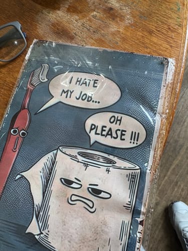 Customer's 'I Hate My Job Oh Please' wall art shown warped and crumpled inside its plastic packaging on a table.