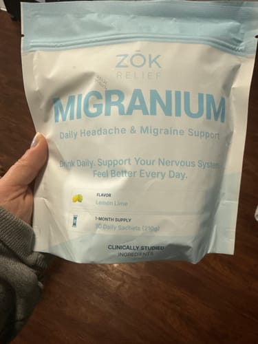 Reviewer holding the white and light blue pouch of Migranium Daily Lemon Lime supplement.