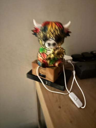 Customer's blurry photo of the colorful Highland Cow LED Night Light lit up on a wooden table.