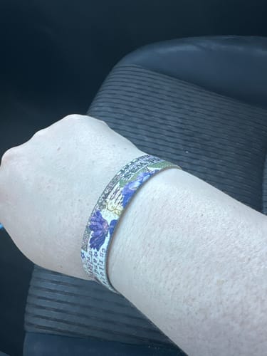 A reviewer wearing the Inkdrinker Bracelet on their wrist, showing the detailed floral and text design.