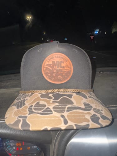 Reviewer's custom rope hat with a black crown and camouflage bill, shown on a car dashboard at night.