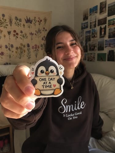 Customer smiling and holding up the 'One Day At A Time' penguin sticker.