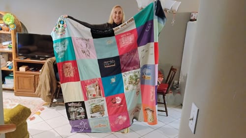 Customer holding up their large, colorful Project Repat T-Shirt Quilt made from memorable old shirts.