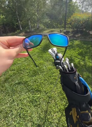Kund som håller i Hovdagolf™-glasögon med blåa linser och en golfbag i bakgrunden.