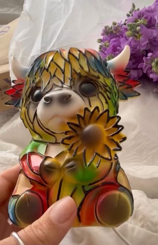 Customer's hand holding the colorful Highland Cow night light figurine, showing its size.