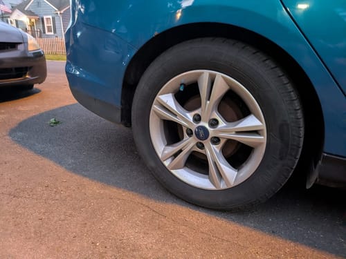 Customer's teal valve stem cap on a car tire, matching the vehicle's teal paint.