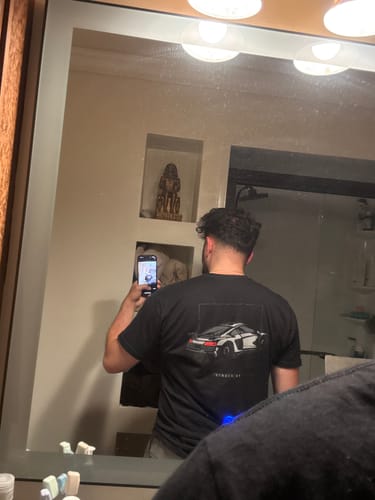 Customer taking a mirror selfie to show the back of the black DCG89 shirt with its white car graphic.