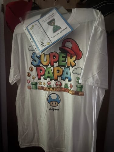Ein Kunde zeigt sein personalisiertes T-Shirt „Super Papa“, das mit dem Namen „Algina“ bedruckt ist.